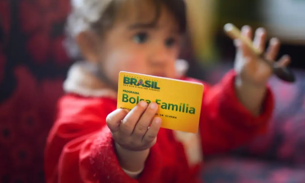 Criança segurando cartão do programa Bolsa Família, destacando o auxílio financeiro para famílias brasileiras.